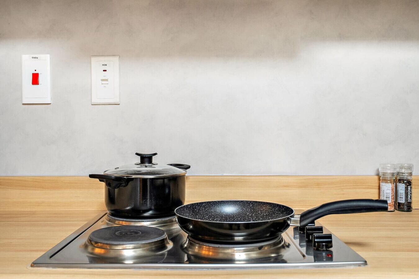 A kitchen with a stove, a pot, and a frying pan. There are two wall switches above the stove, one labeled "Oven" and the other "HOB."
