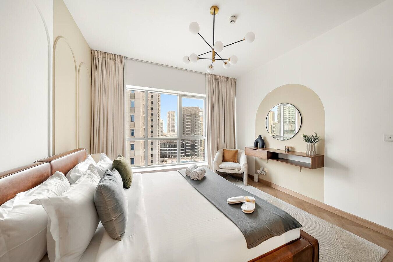 Une chambre d’hôtel moderne dotée d’un grand lit, d’un coin salon, d’une coiffeuse et offrant une vue sur le paysage urbain.
