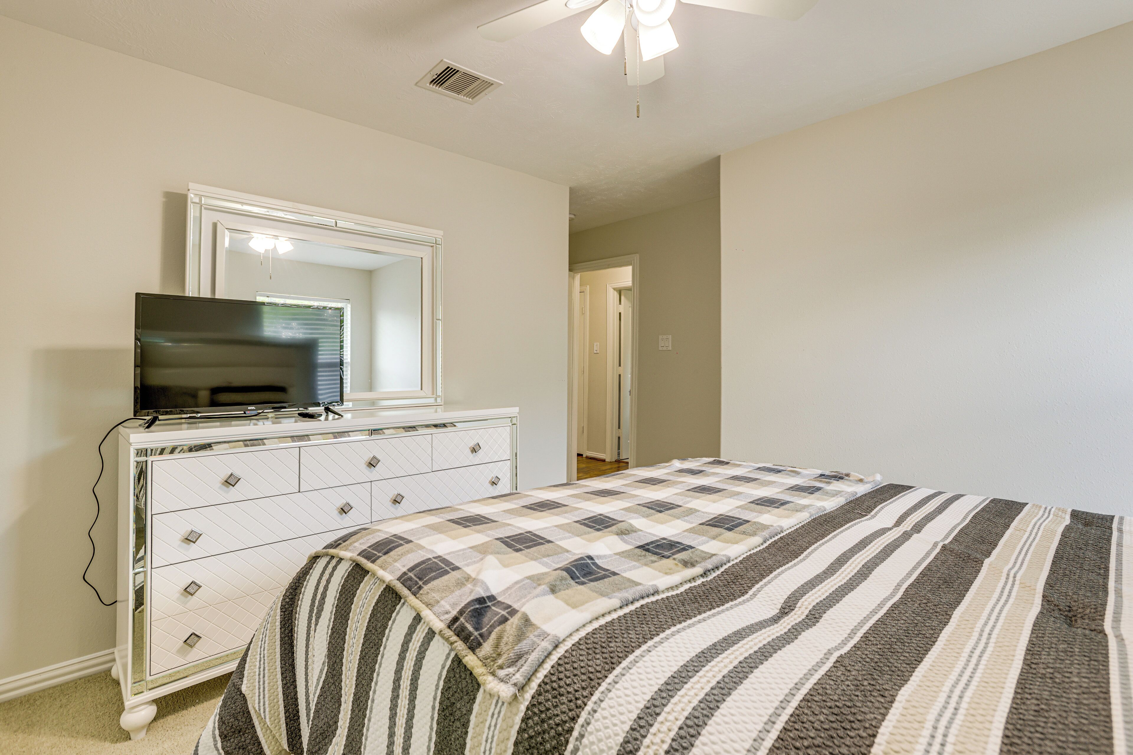 A bedroom with a bed, dresser, television, and a ceiling fan.