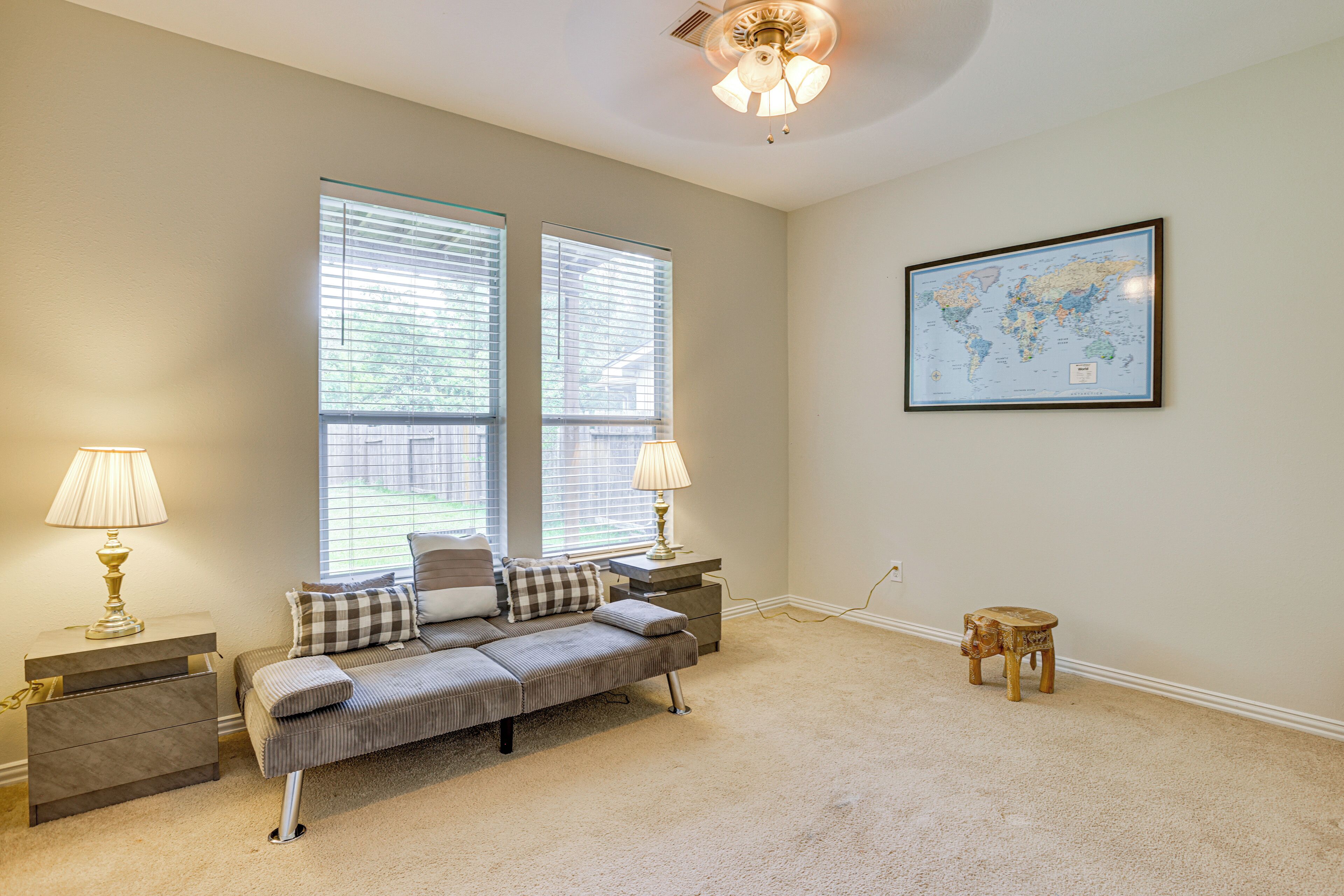 A bedroom with a bed, two bedside tables with lamps, a small wooden stool, and a world map on the wall.