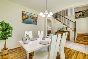 Un coin repas avec une table blanche dressée pour quatre personnes, un lustre et un escalier menant à l’étage supérieur.