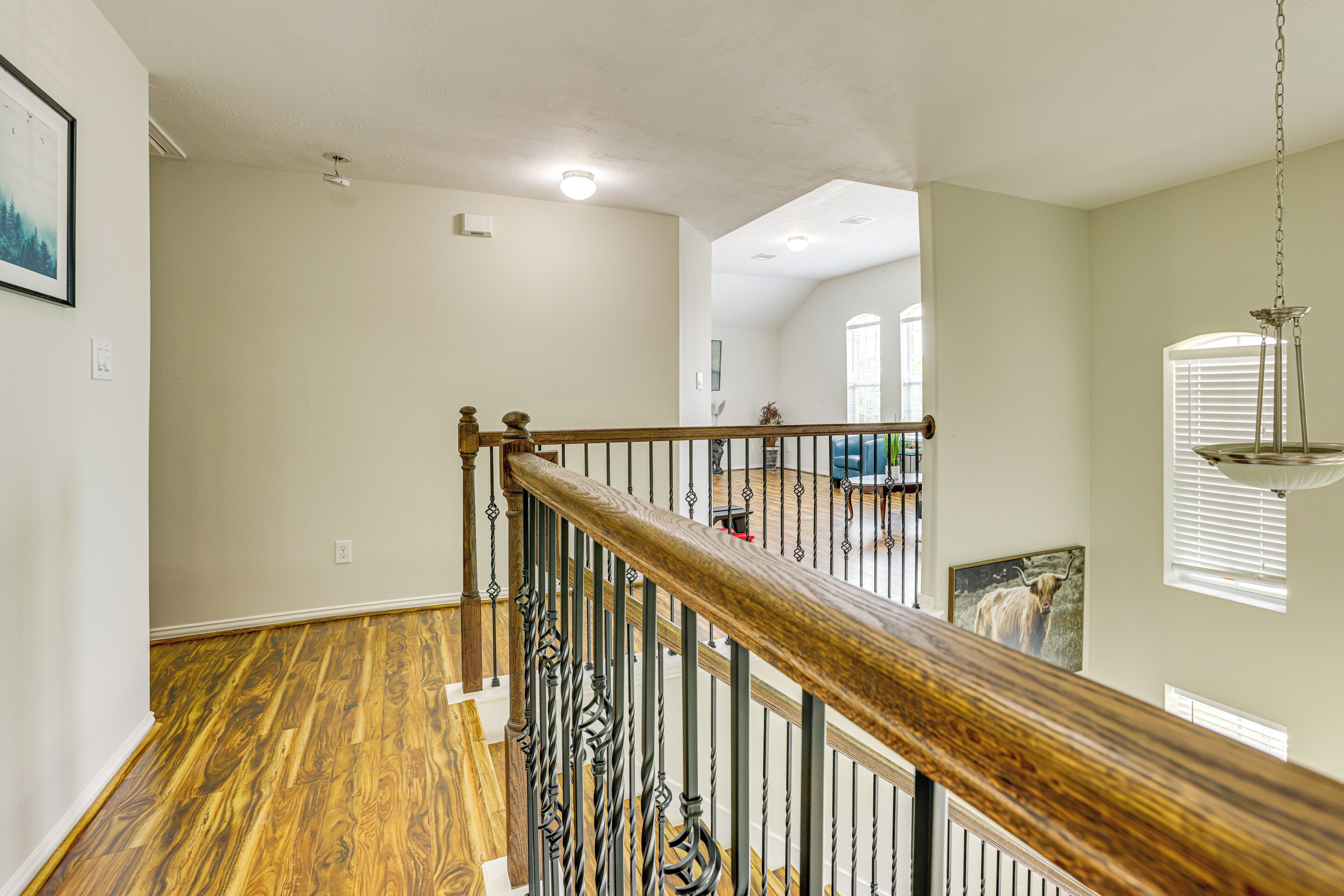 A spacious living area with hardwood flooring, a wooden staircase with a metal railing, and a hanging light fixture.