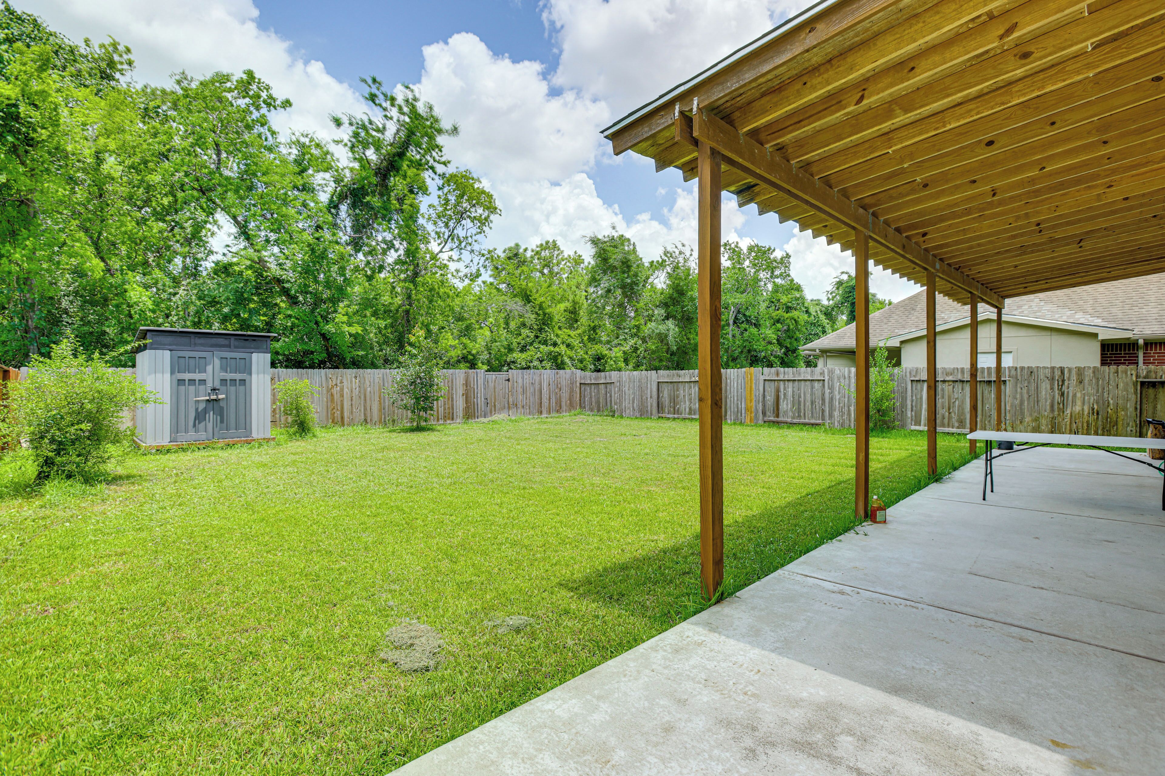 A backyard with a wooden pergola, a small shed, and a concrete patio area.