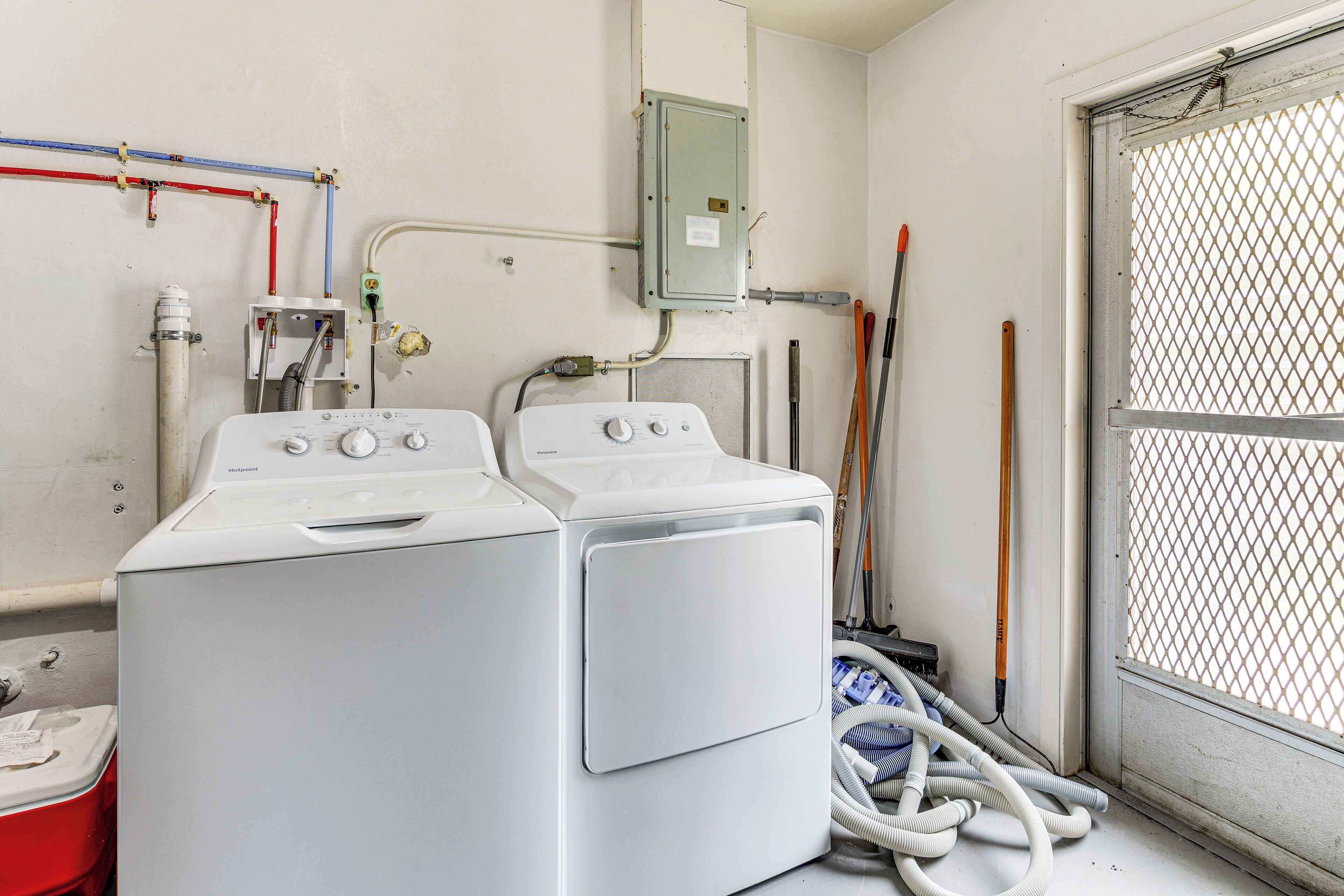 A laundry room with two washing machines, a utility meter, and various pipes and hoses.