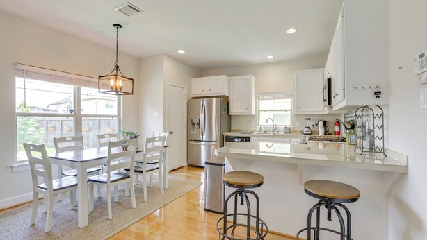 A modern kitchen with white cabinetry, a stainless steel refrigerator, and a dining area with a table and chairs.