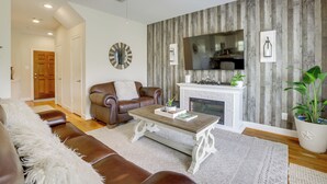 A living room with a brown leather sofa, a coffee table, a fireplace, and a television mounted on a wooden wall.