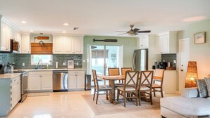A modern kitchen with white cabinets, a stainless steel dishwasher, and a dining area with wooden chairs and a table.