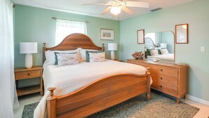 A bedroom with a wooden bed, a nightstand with a lamp, a dresser with a mirror, and a ceiling fan.