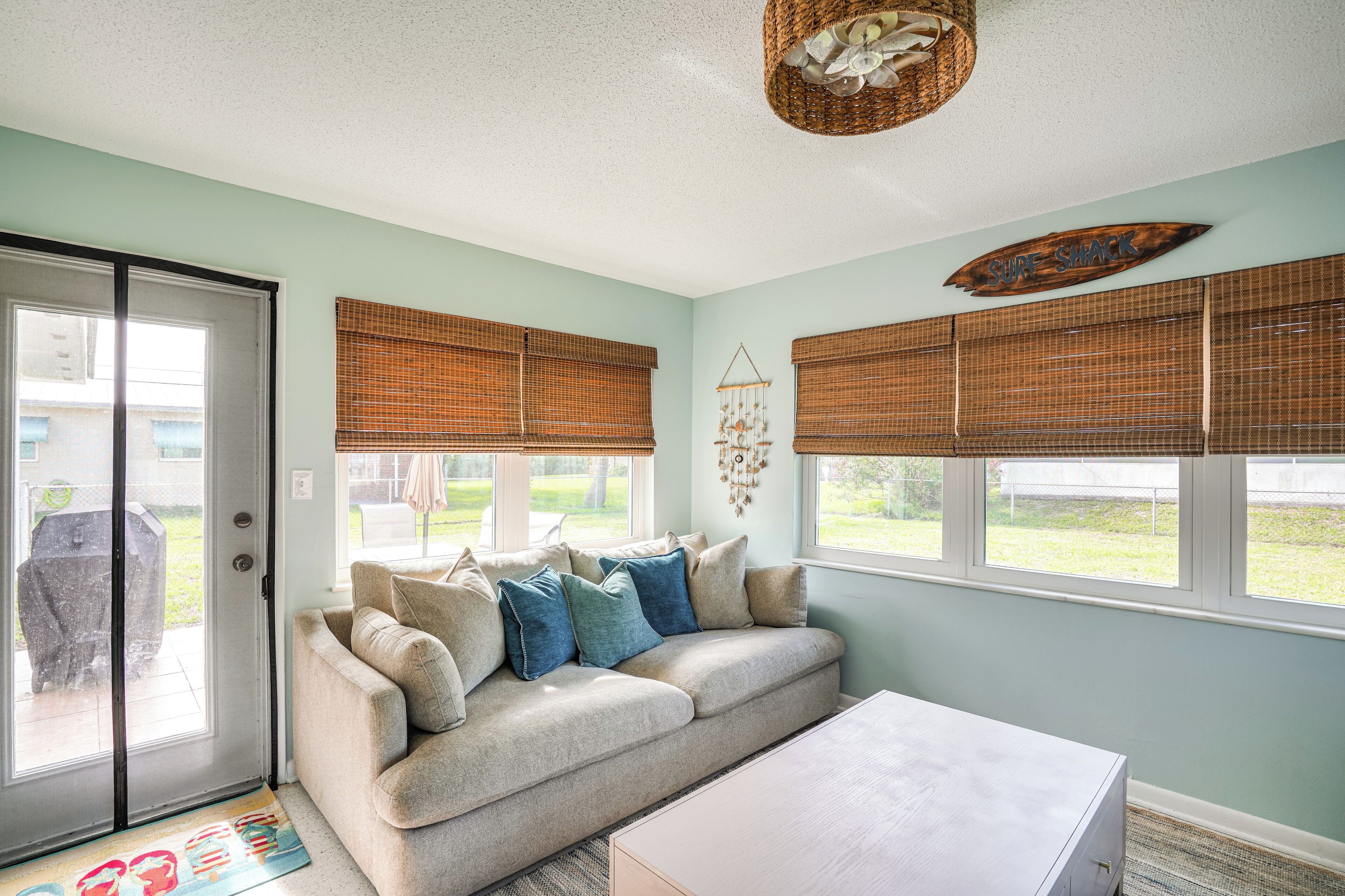 A living room with a beige sofa, a white coffee table, and a large window with blinds.