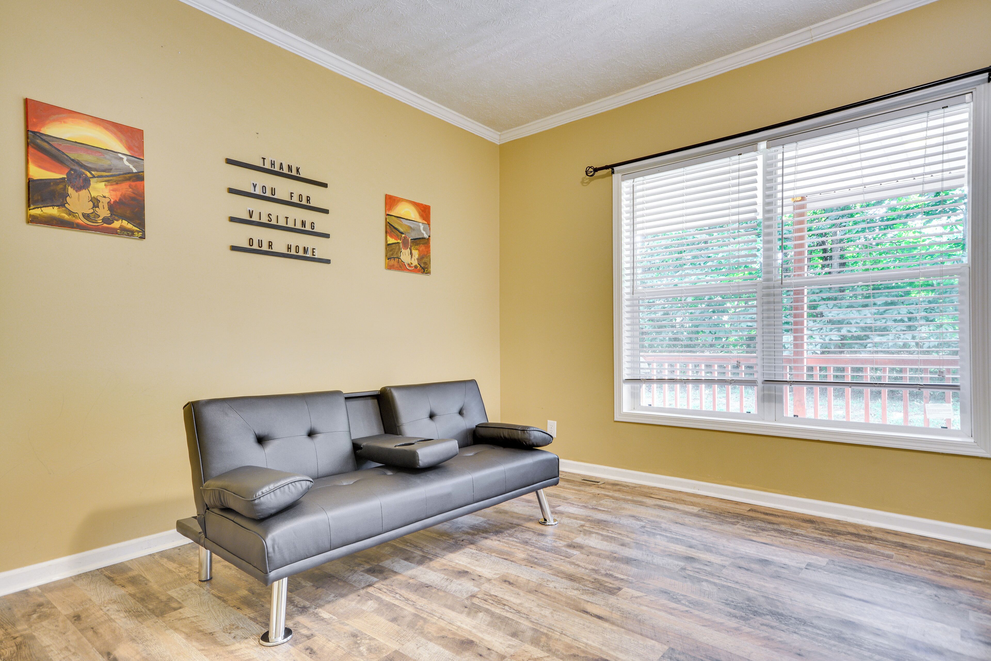 Ein Wohnzimmer mit einem schwarzen Ledersofa, Holzböden und einem großen Fenster mit Jalousien.