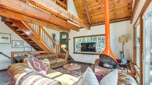 Ein geräumiges Wohnzimmer mit hoher Holzbalkendecke, einer Treppe und einem großen Fenster.