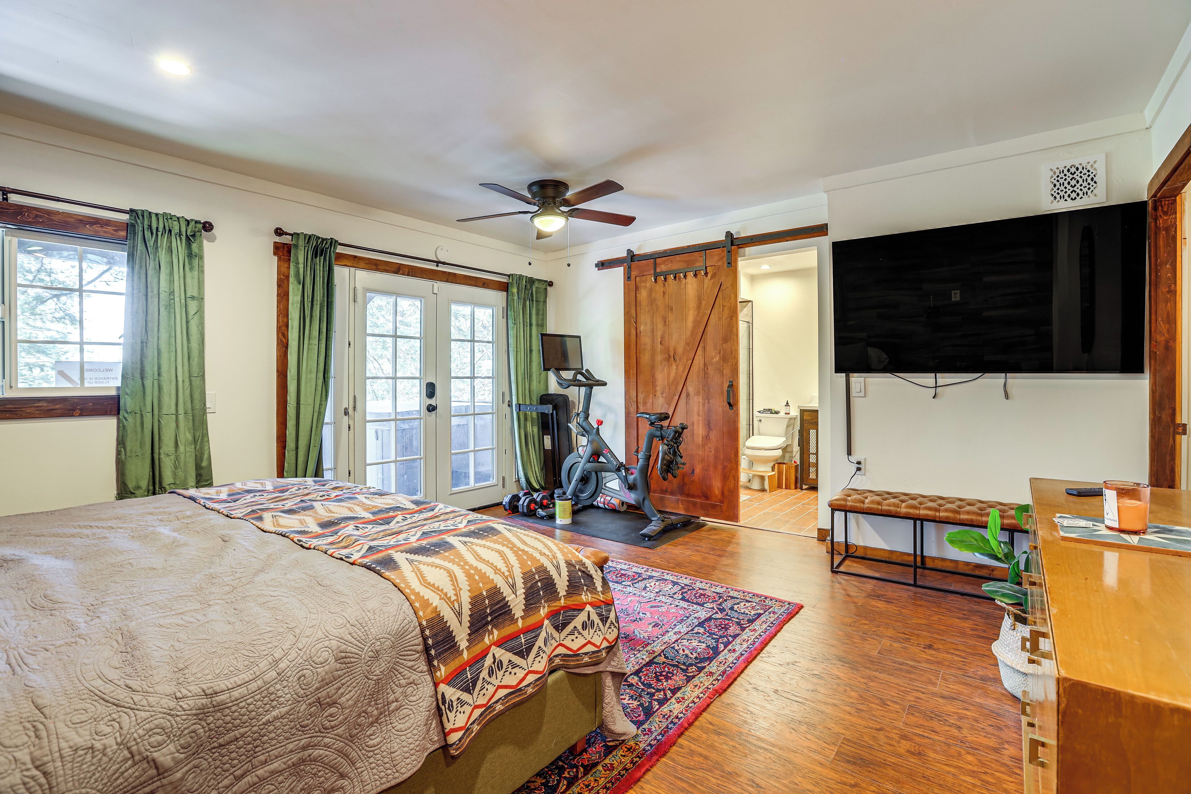 A bedroom with a bed, a desk, a television, a ceiling fan, and a sliding door.