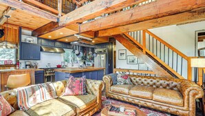 Ein großzügiger Wohnbereich mit Ledersofas, einer Holztreppe und einer Küche im Hintergrund.