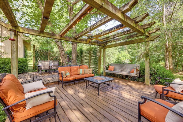 Eine Holzterrasse mit Gartenmöbeln, darunter eine Sitzecke mit Sofa und Stühlen, unter einer Pergola.