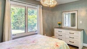 A bedroom with a large bed, a dresser, a mirror, and a window with curtains.