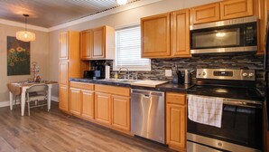 A modern kitchen with wooden cabinets, stainless steel appliances, and a dining area with a table and chairs. - 3 Mi to Shops & Eats in Uptown: Greenwood Studio (Greenwood)