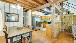 A rustic kitchen with wooden beams, a stainless steel refrigerator, and a dining area with a wooden table and chairs. - Serene Hill Country Home! Hike, Sleep, Unplug! (Kerrville)