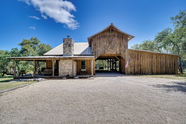 Un bâtiment de style rustique, évoquant une grange, avec une cheminée en pierre, un revêtement extérieur en bois et une allée gravillonnée.
