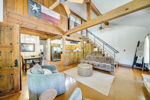 Un vaste espace de vie doté d’un plafond haut, de poutres en bois, d’un escalier et d’une cuisine située au fond de la pièce.