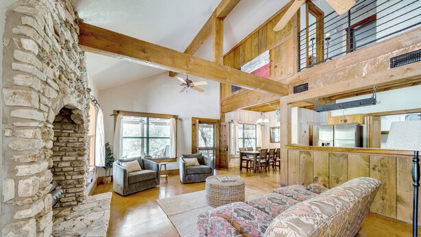 A spacious living area with a stone fireplace, wooden beams, and a large sofa. - Serene Hill Country Home! Hike, Sleep, Unplug! (Kerrville)