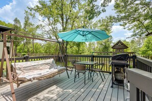 Eine Holzterrasse mit einer Schaukel, einem Tisch mit Stühlen, einem Grill und einem Sonnenschirm.