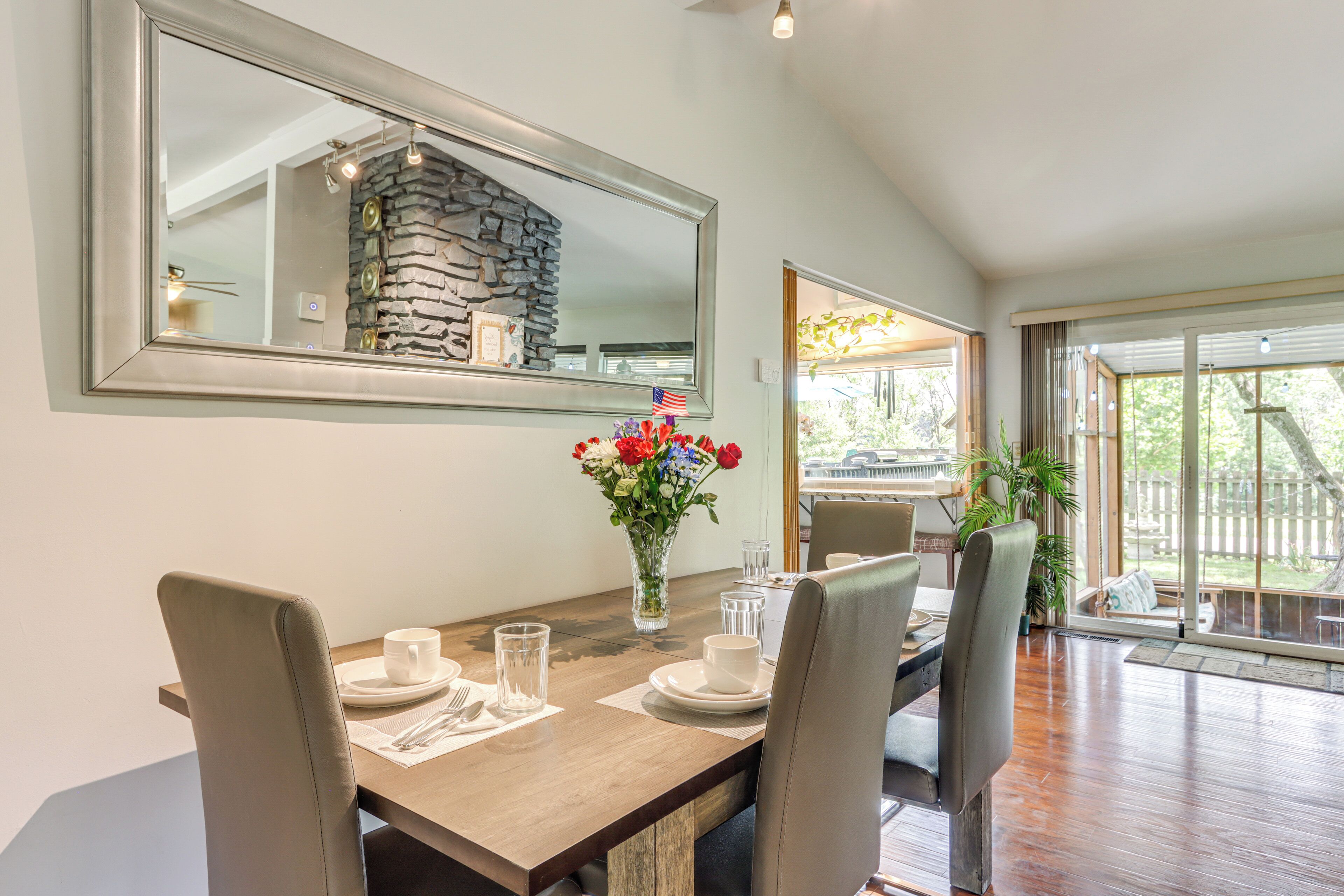 A dining area with a wooden table, four chairs, a vase with flowers, and a large mirror on the wall.