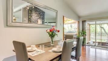A dining area with a wooden table, four chairs, a vase with flowers, and a large mirror on the wall.