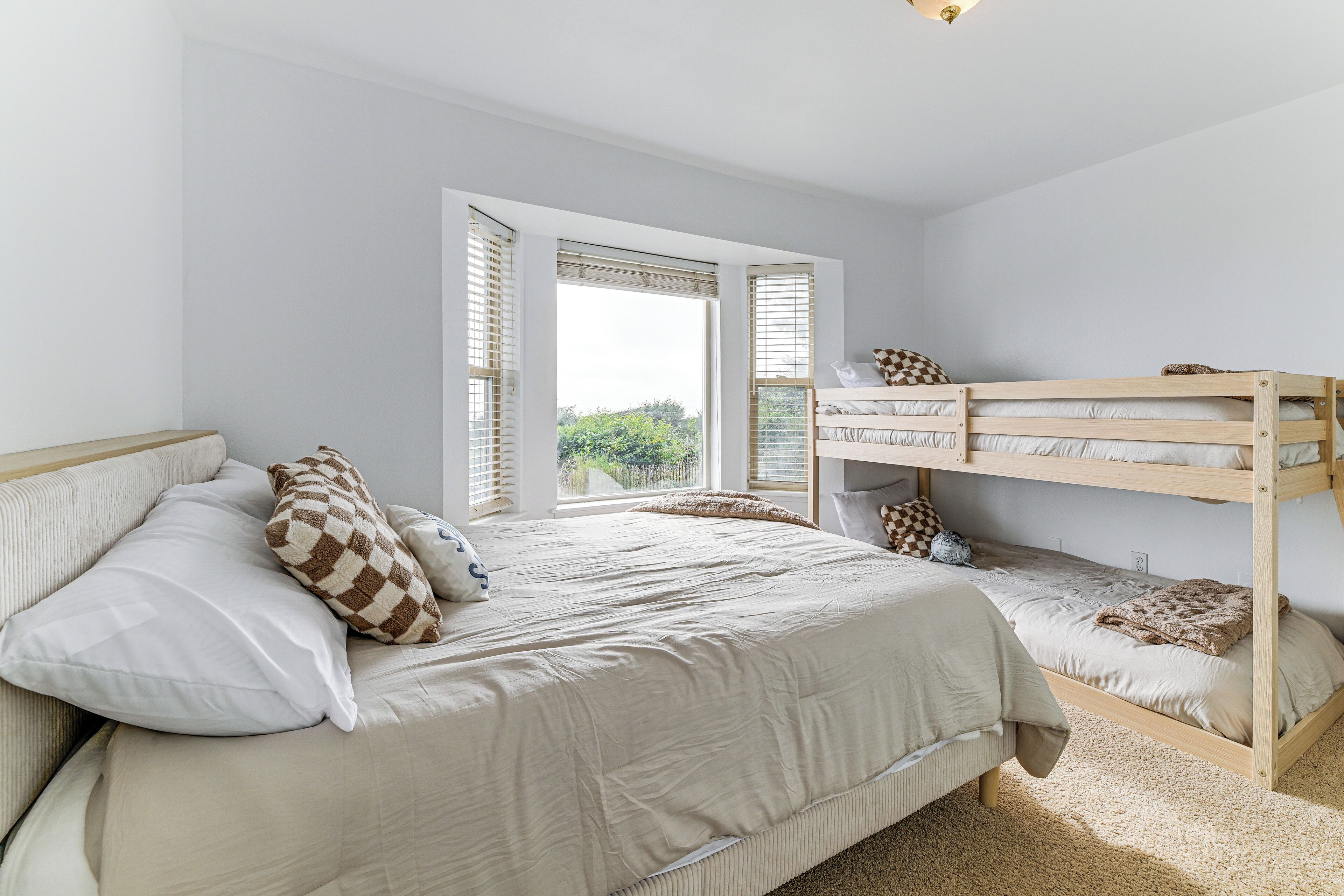 Un dormitorio con una cama grande, una litera y un ventanal con persianas.