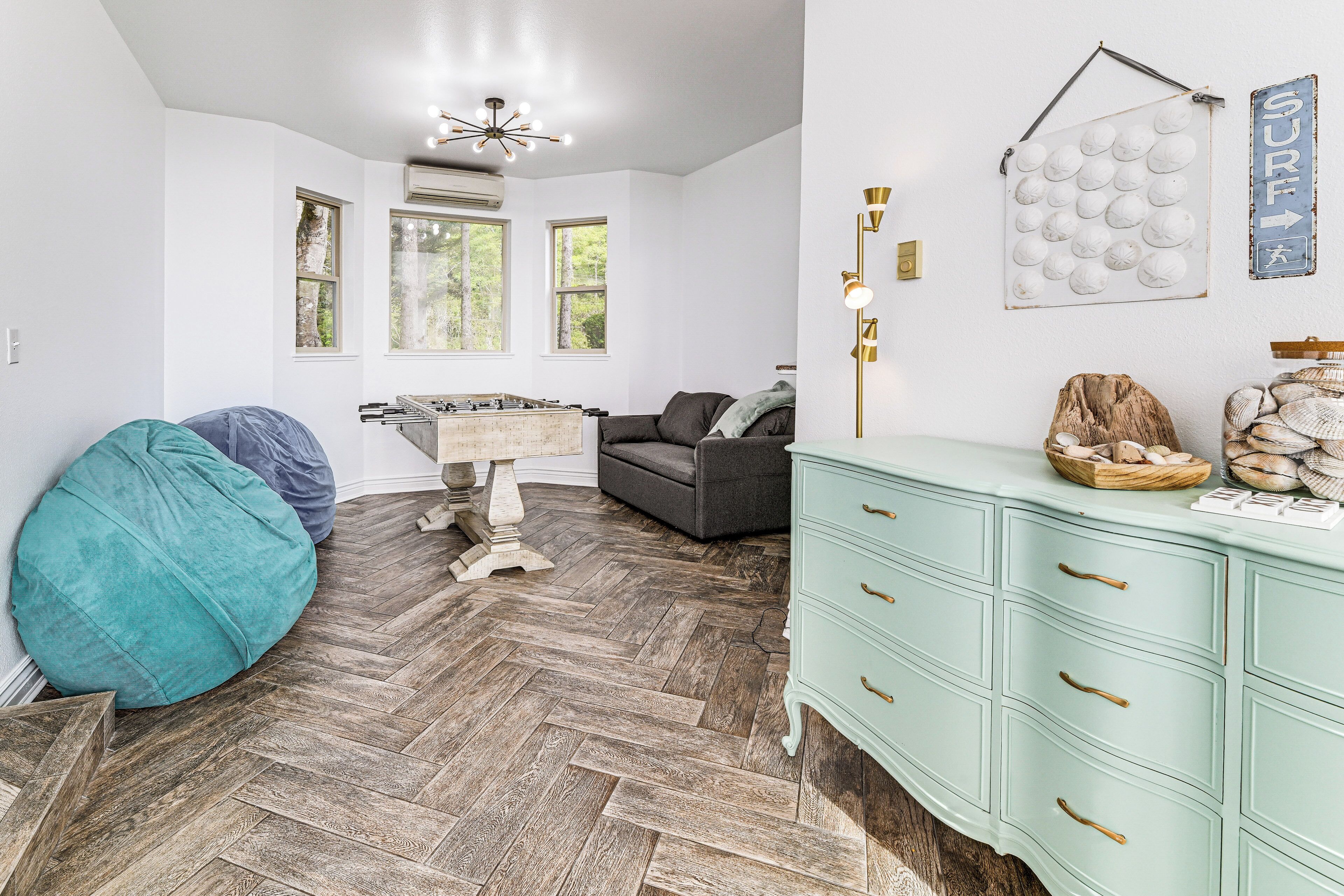 Ein Zimmer mit Fischgrätparkett, einem blauen Sitzsack, einem grauen Sofa, einer hellblauen Kommode und einem wandmontierten Globus.