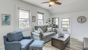 A spacious living room with a grey sofa, a blue armchair, and a wooden coffee table. - Stroll to Ocean Grove Boardwalk & Beach: Sleek Apt (Ocean Grove)