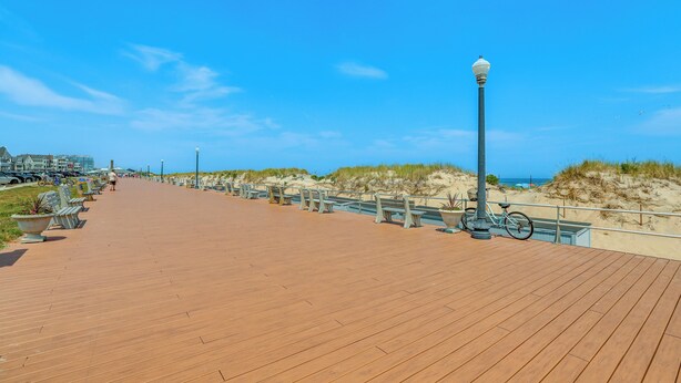 A wooden boardwalk with benches and a lamp post, leading to a sandy beach area. - Stroll to Ocean Grove Boardwalk & Beach: Sleek Apt (Ocean Grove)