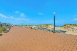 Una passerella in legno con panchine e un lampione, che conduce a una spiaggia sabbiosa.