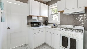 A compact kitchen with white cabinets, a gas stove, a microwave, and a coffee maker. - Stroll to Ocean Grove Boardwalk & Beach: Sleek Apt (Ocean Grove)