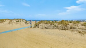 A sandy beach with a wooden fence and a blue pathway leading to the water. - Stroll to Ocean Grove Boardwalk & Beach: Sleek Apt (Ocean Grove)