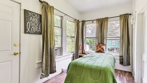 A room with a bed, a window with curtains, a door with a sign, and a view of a house outside. - Home w/ Yard - Close to Hospitals, Dtwn Shreveport (Shreveport)
