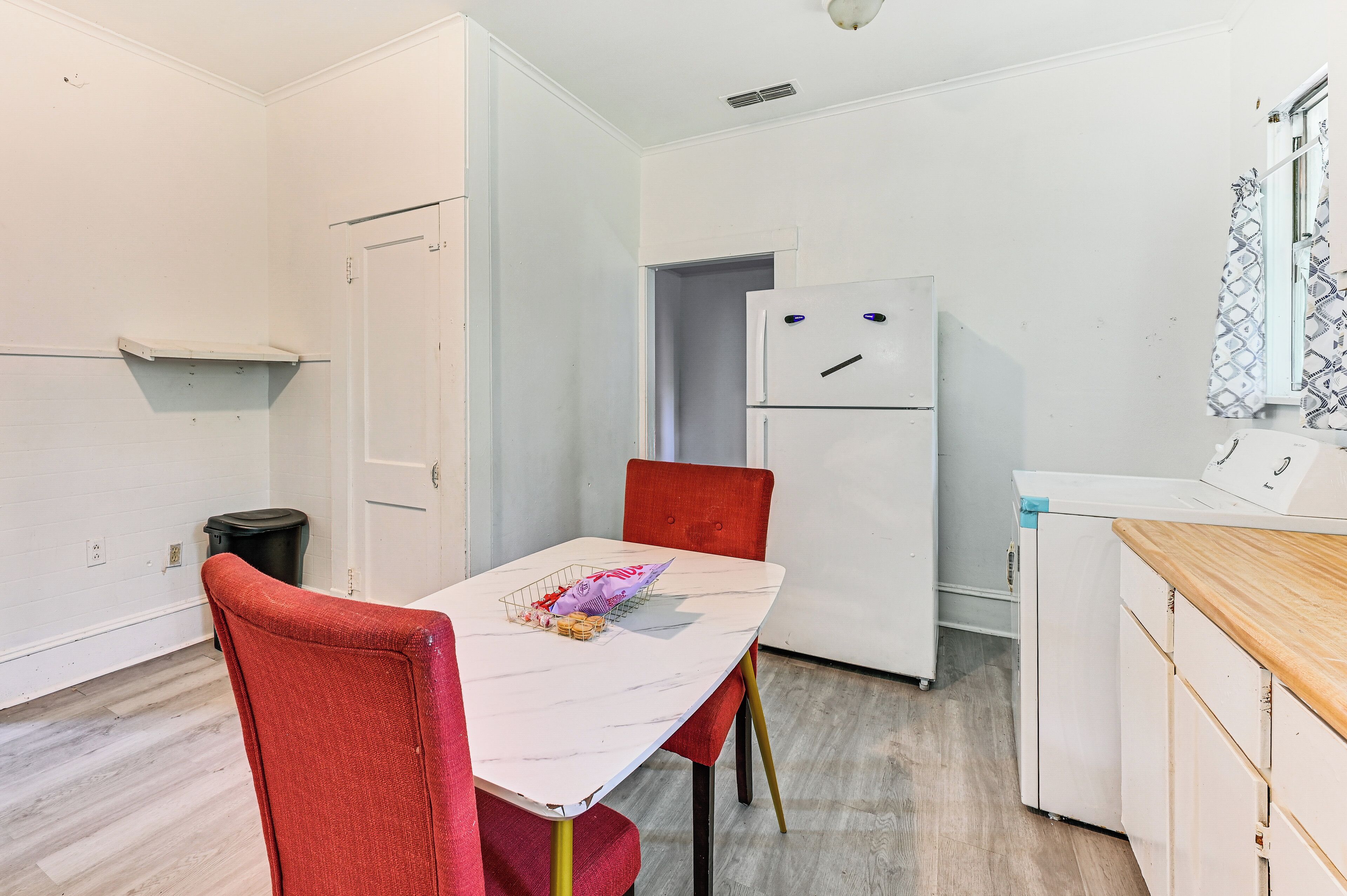 A compact kitchen with white cabinets, a white refrigerator, a red chair, and a marble table.