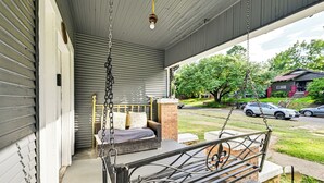 A porch with a swing, a brick wall, and a view of a residential street. - Home w/ Yard - Close to Hospitals, Dtwn Shreveport (Shreveport)