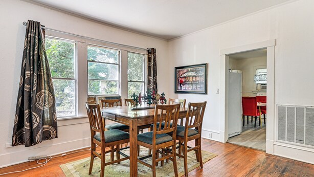 A dining area with a wooden table and chairs, large windows, and a kitchen visible through an open door. - Home w/ Yard - Close to Hospitals, Dtwn Shreveport (Shreveport)