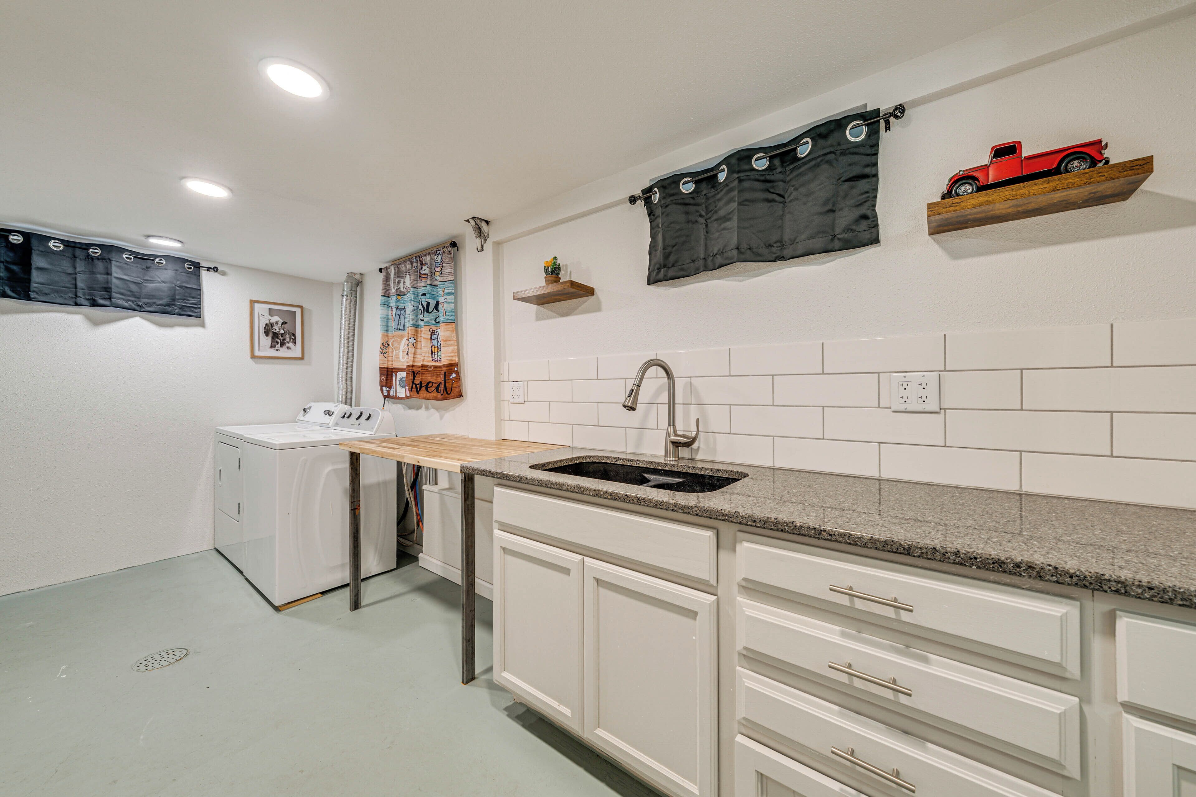 A compact kitchen with white cabinets, a granite countertop, a sink, and a washing machine.