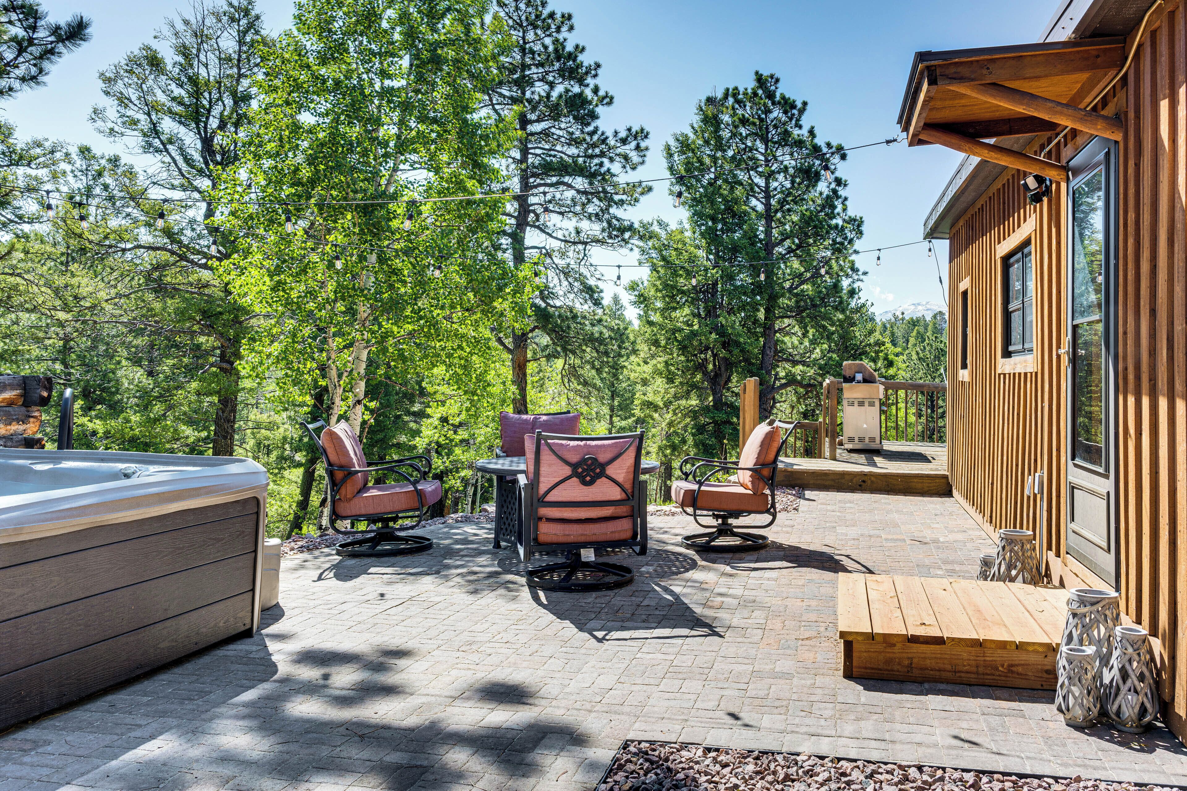 Una cabaña de madera con jacuzzi, mobiliario exterior y una terraza con vistas a un bosque.