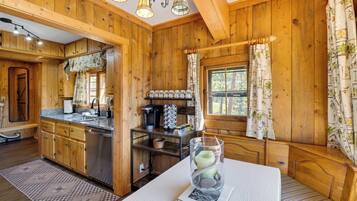 Interior de uma cabana de madeira, com cozinha, área de refeições e um espaço de estar aconchegante.