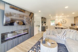 Una sala de estar moderna con un televisor de pantalla plana grande, un sofá gris, una mesa de centro y una cocina al fondo.