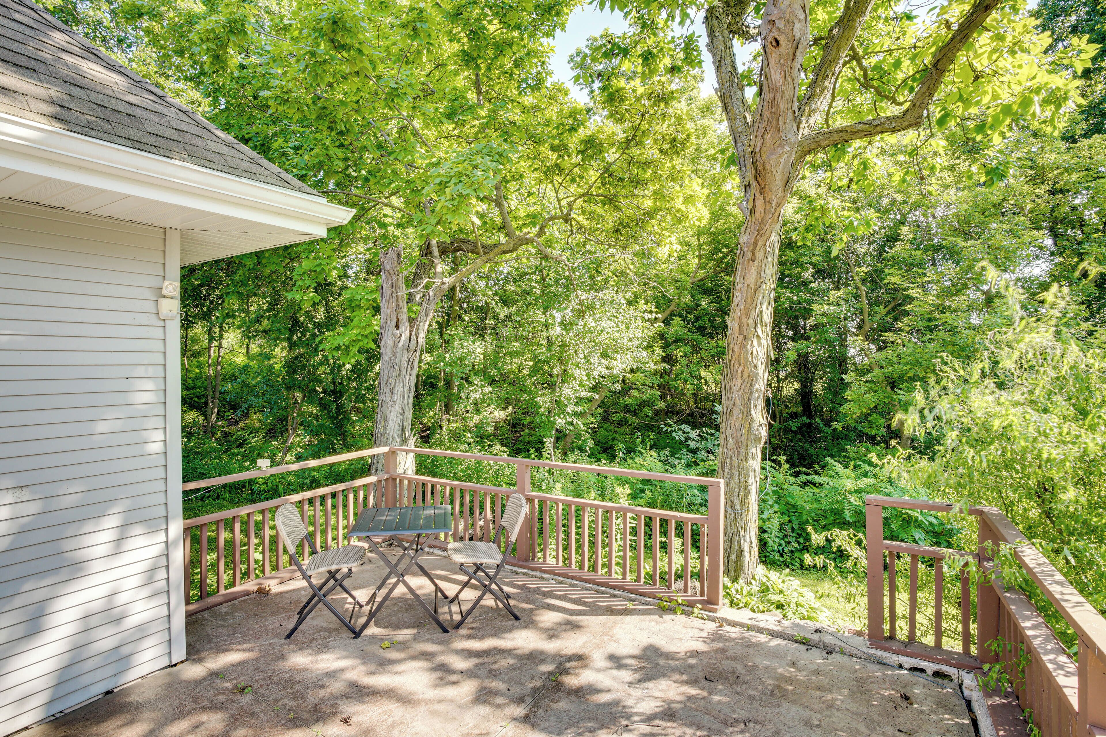 A covered outdoor area with a table and chairs, surrounded by trees and a wooden railing.