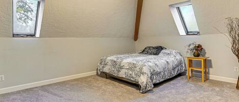 A bedroom with a bed, two skylights, a nightstand, and a vase with flowers.