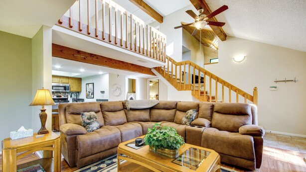 A spacious living room with a brown leather sectional sofa, a wooden coffee table, and a staircase with a wooden railing leading to an upper level. - Walk to Pomme de Terre Lake: Pet-friendly Escape (Flemington)