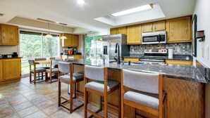 A modern kitchen with wooden cabinets, a stainless steel refrigerator, a microwave, and a large island with bar stools. - Walk to Pomme de Terre Lake: Pet-friendly Escape (Flemington)