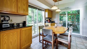 A kitchen with wooden cabinets, a dining table with chairs, and a view of the outdoors through large windows. - Walk to Pomme de Terre Lake: Pet-friendly Escape (Flemington)