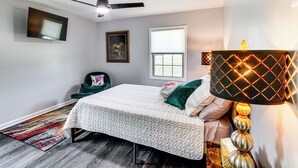 A bedroom with a bed, a ceiling fan, a window, a framed picture, and a bedside lamp.