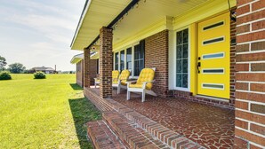 A brick house with a yellow door and a porch with two chairs.
