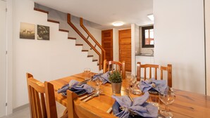 Ein Essbereich mit einem Holztisch, gedeckt für vier Personen, einer Treppe und einem Küchenbereich im Hintergrund.